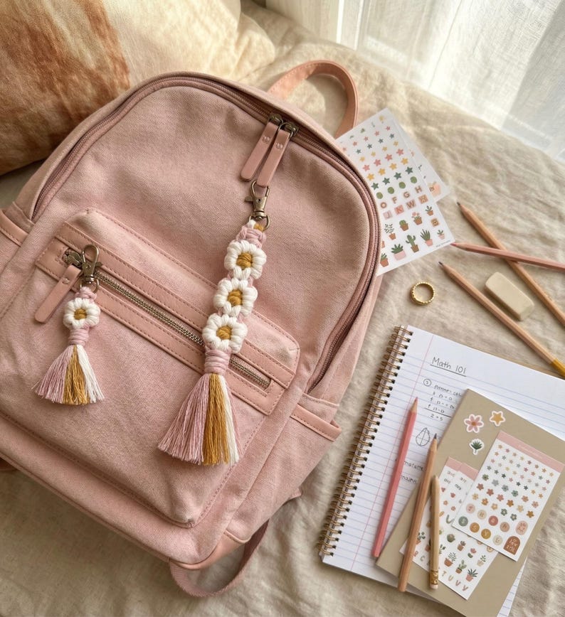 Handcrafted daisy macrame keychain clipped to a backpack, boho zipper charm made from cotton cord with floral pattern and tassel.