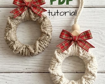 May include: Two circular ornaments made of wrapped yarn, one in tan and one in off-white, each featuring a red and green plaid ribbon bow, a wooden bead, and a hanging cord. The text PDF tutorial is visible in green and black lettering.