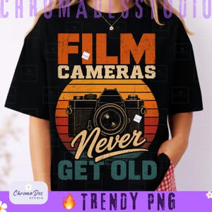Op de afbeelding: Zwart T-shirt met een vintage camera ontwerp en de tekst "FILM CAMERAS Never GET OLD." Het ontwerp bevat een oranje, gele en rode zonsondergang grafiek. Het T-shirt heeft een klassieke ronde hals.
