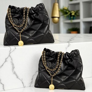 Puede incluir: Dos bolsos negros acolchados con correas de cadena doradas y colgantes de monedas. Los bolsos tienen un cierre de cord&oacute;n y un patr&oacute;n de diamantes. El texto "CLASSIC DESIGN" es visible en la parte inferior de los bolsos.