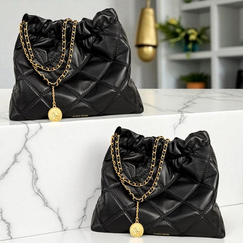 Puede incluir: Dos bolsos negros acolchados con correas de cadena doradas y colgantes de monedas. Los bolsos tienen un cierre de cord&oacute;n y un patr&oacute;n de diamantes. El texto "CLASSIC DESIGN" es visible en la parte inferior de los bolsos.