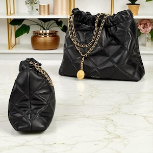 Puede incluir: Dos bolsos de mano de cuero negro acolchado con correas de cadena doradas. Un bolso es m&aacute;s grande con cierre de cord&oacute;n, y el otro es m&aacute;s peque&ntilde;o. Ambos bolsos tienen un dije de moneda dorada.