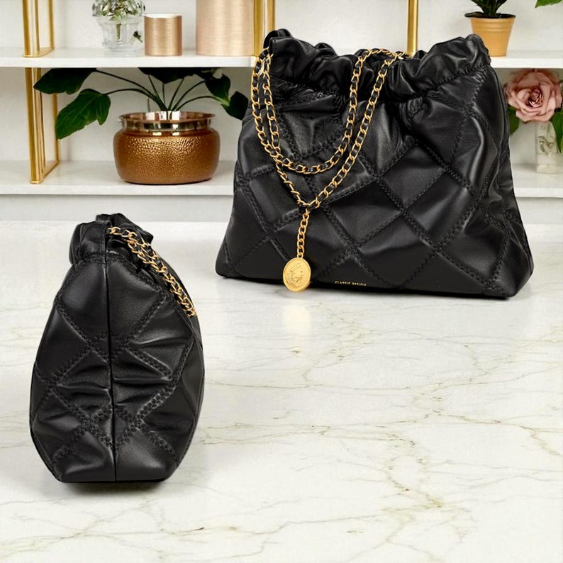 Puede incluir: Dos bolsos de mano de cuero negro acolchado con correas de cadena doradas. Un bolso es m&aacute;s grande con cierre de cord&oacute;n, y el otro es m&aacute;s peque&ntilde;o. Ambos bolsos tienen un dije de moneda dorada.