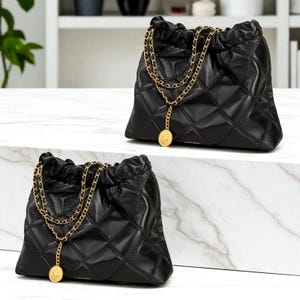 Puede incluir: Dos bolsos de mano de cuero negro acolchado con correas de cadena doradas y colgantes de monedas. Los bolsos tienen un cierre de cord&oacute;n y un patr&oacute;n de diamantes. Los bolsos se exhiben sobre una superficie de m&aacute;rmol blanco.