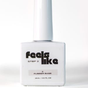 May include: A white nail product bottle with a long, rectangular cap. The bottle has the words "feels like" in black, with "STEP 2" below. It also says "RUBBER BASE" and "15ML / 0.5 FL OZ".