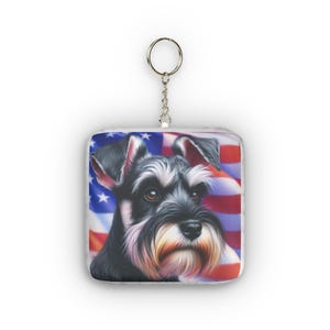 May include: A square keyring featuring a detailed illustration of a black and silver Schnauzer dog against a backdrop of the American flag. The keyring includes a silver-toned metal split ring attached to a short chain at the top centre.