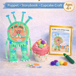 May include: A 3-in-1 Story Craft Kit with a puppet, storybook, and cupcake craft. The image shows a green monster puppet, a pink cupcake, and a framed illustration titled "Blobby & The Cupcake Chase". Includes a green crayon.