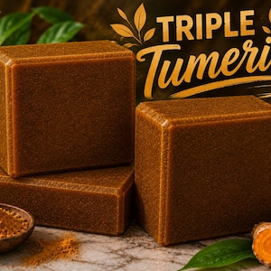 May include: Three rectangular bars of brown turmeric soap are arranged with a small wooden bowl containing turmeric powder. The text "TRIPLE Tumeric" is displayed in a stylized gold font above the soap bars, accompanied by turmeric roots.