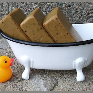 May include: A white, claw-foot bathtub filled with four rectangular bars of soap. The soap is light brown with dark flecks. A yellow rubber duck with an orange beak sits beside the tub.