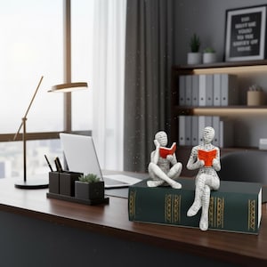 以下が含まれることがあります： 赤い本を読んでいる白とグレーの2体のフィギュアが、大きな緑の本の上に座っています。フィギュアは、ラップトップ、デスクオーガナイザー、モダンなランプを備えた濃い木製の机の上にあります。背景には窓と棚があります。