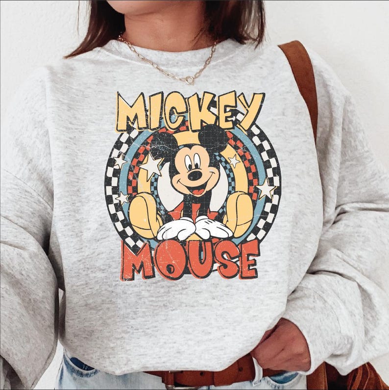 K&ouml;nnte beinhalten: Hellgraues Sweatshirt mit einem Mickey Mouse-Motiv im Vintage-Stil. Die Grafik enth&auml;lt die Worte "MICKEY MOUSE" in Gelb und Rot, mit Mickey in der Mitte. Das Design hat einen Retro-Look.