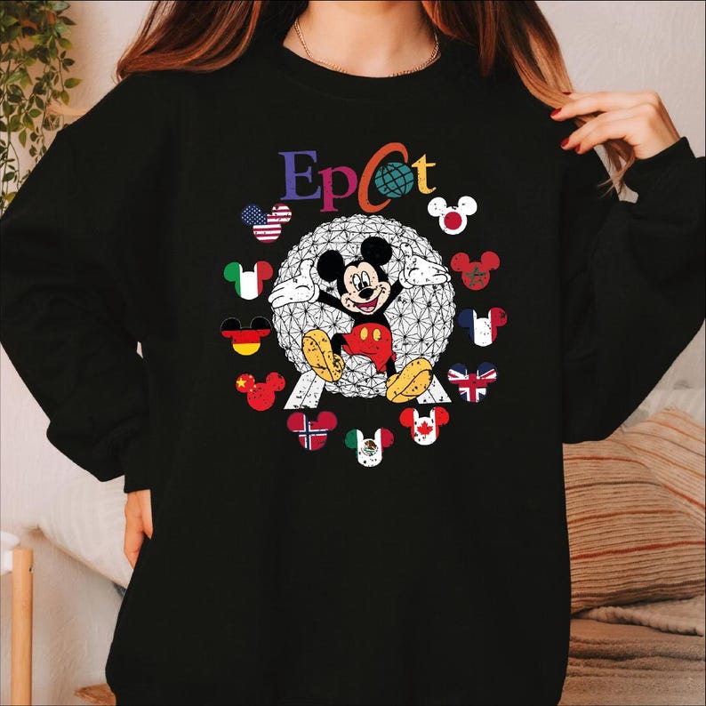 May include: Black sweatshirt featuring the word "Epcot" in colorful letters. The design includes a geometric sphere with Mickey Mouse in the center, surrounded by flags and Mickey Mouse icons representing different countries. A fun and colorful design.