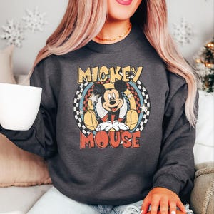 K&ouml;nnte beinhalten: Dunkelgraues Sweatshirt mit einem Mickey Mouse-Motiv im Vintage-Stil. Die Grafik enth&auml;lt die Worte "Mickey Mouse" in einer Retro-Schrift, mit Mickey Mouse in der Mitte. Das Sweatshirt hat einen Rundhalsausschnitt.