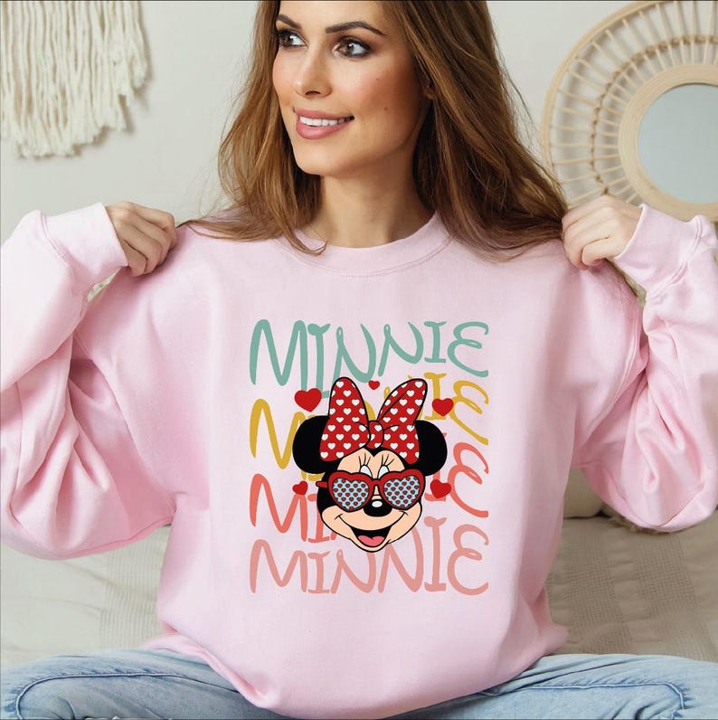 Puede incluir: Sudadera rosa claro con un dise&ntilde;o de Minnie Mouse. El dise&ntilde;o incluye un lazo rojo con lunares, gafas de sol y la palabra "MINNIE" en varios colores. La sudadera es de cuello redondo.