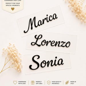 Può includere: Tre targhe rettangolari in acrilico trasparente con i nomi Marica, Lorenzo e Sonia in corsivo nero. Ogni targa mostra un nome in un carattere corsivo in grassetto. Le targhe sono disposte in una pila verticale sfalsata e sovrapposta.