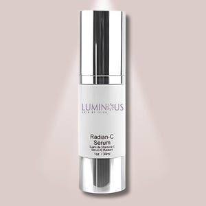 Op de afbeelding: Een zilveren en witte Radian-C Serumfles met de tekst "LUMINUS SKIN BY JAIRA" en "Radian-C Serum" in het zwart. De fles bevat 30 ml serum. De achtergrond is zachtroze.