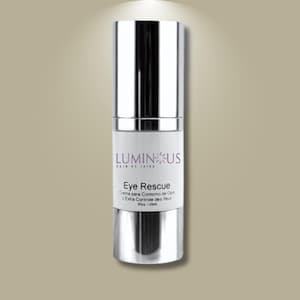 Puede incluir: Botella cilíndrica de crema para ojos con tapa y base plateadas, y una etiqueta blanca. La etiqueta presenta el texto "LUMINOUS SKIN BY JAFRA" y "Eye Rescue" en inglés, con texto adicional en español y francés. La botella contiene 20 ml.