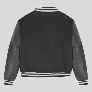 Op de afbeelding: Een zwart varsity-jack met lange mouwen met een gladde textuur, een geribbelde kraag, boorden en zoom met witte strepen. Het jack heeft een effen zwart lichaam en bijpassende zwarte mouwen, wat zorgt voor een klassiek en sportief ontwerp.