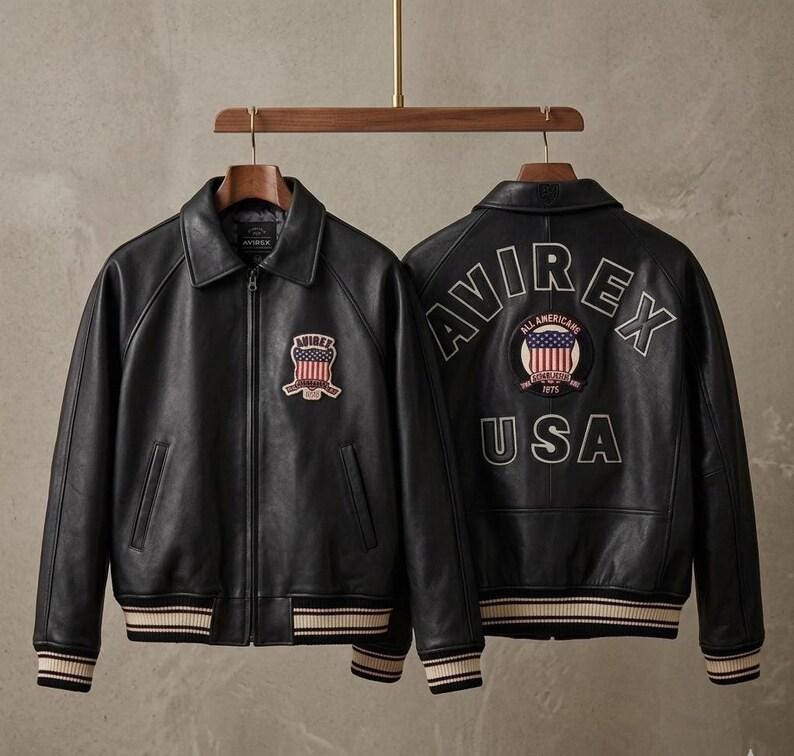 May include: A black leather jacket with a front zipper, a collar, and striped ribbed cuffs and hem. The front features an Avirex patch with a flag design. The back displays the text Avirex and USA with a circular patch featuring a flag and text.