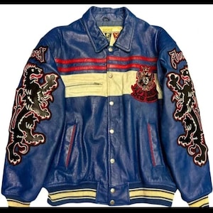 May include: Blue leather jacket with red and cream stripes. Features black lion appliques on the sleeves and a crest patch. The jacket has a button-up front and a ribbed hem.