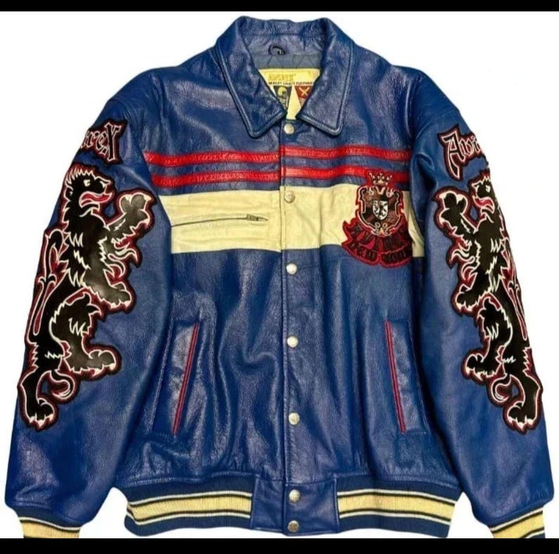May include: Blue leather jacket with red and cream stripes. Features black lion appliques on the sleeves and a crest patch. The jacket has a button-up front and a ribbed hem.