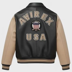 Puede incluir: Una chaqueta tipo varsity negra y beige con el texto AVIREX y USA en letras beige en la espalda. Un parche circular con un gr&aacute;fico de la bandera estadounidense y el texto OLD AMERICAN 1975 est&aacute; centrado entre las palabras. La chaqueta tiene cuello y pu&ntilde;os.