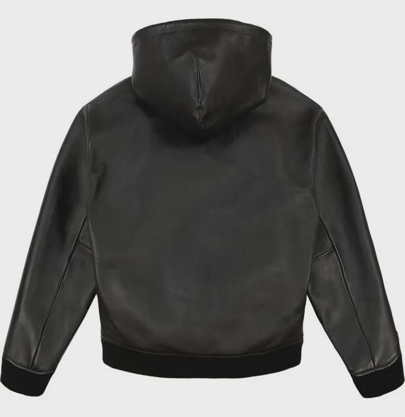 May include: Black leather jacket with a hood. The jacket has long sleeves and a black ribbed hem and cuffs. The back view shows the hood and the smooth texture of the leather. A classic outerwear piece.