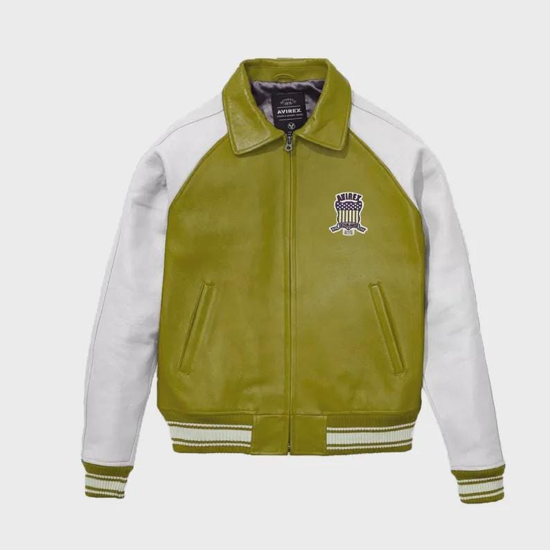 May include: Olive green leather jacket with white sleeves and collar. Features a zip-up front, side pockets, and a striped hem and cuffs. The jacket has a patch on the chest with the text "AVIREX".