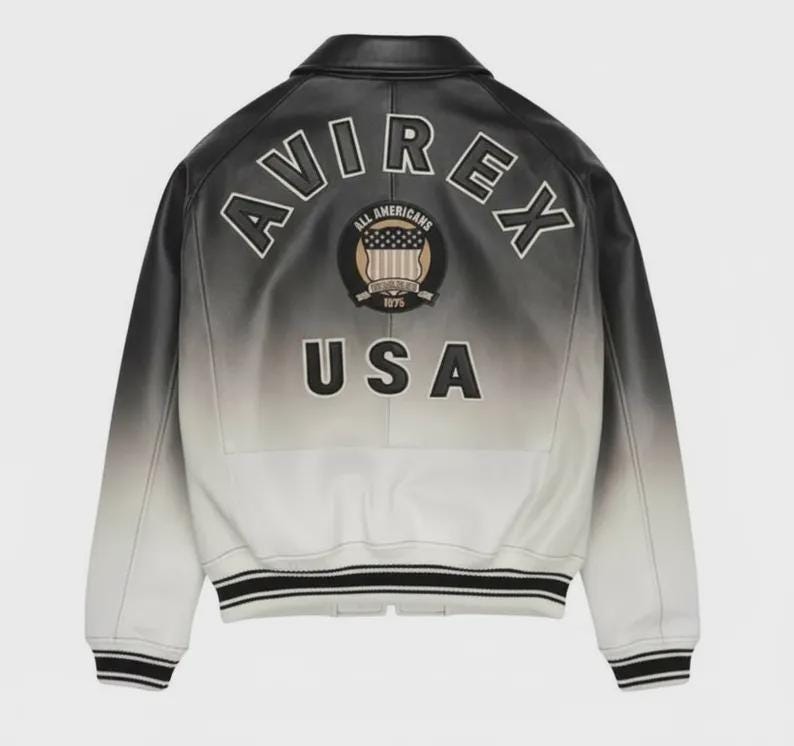 May include: A black and white gradient leather bomber jacket featuring the text AVIREX in an arc, a circular All Americans 1975 patch with a shield graphic, and the text USA in large black letters on the back, with striped ribbed cuffs and hem.