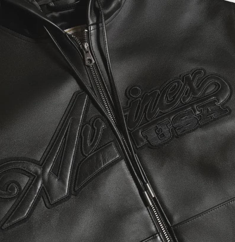 May include: Black leather jacket with a full zipper closure. The jacket features the word "Avirex" in a stylized font, with "USA" underneath. The jacket has a classic bomber style.