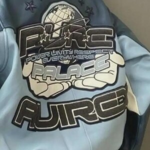 May include: A light blue and navy blue leather jacket with a large graphic on the back. The graphic includes the words "PURE PALACE" and "POWER UNITY RESPECT EVERYWHERE" in a stylized font, along with a globe and stars.