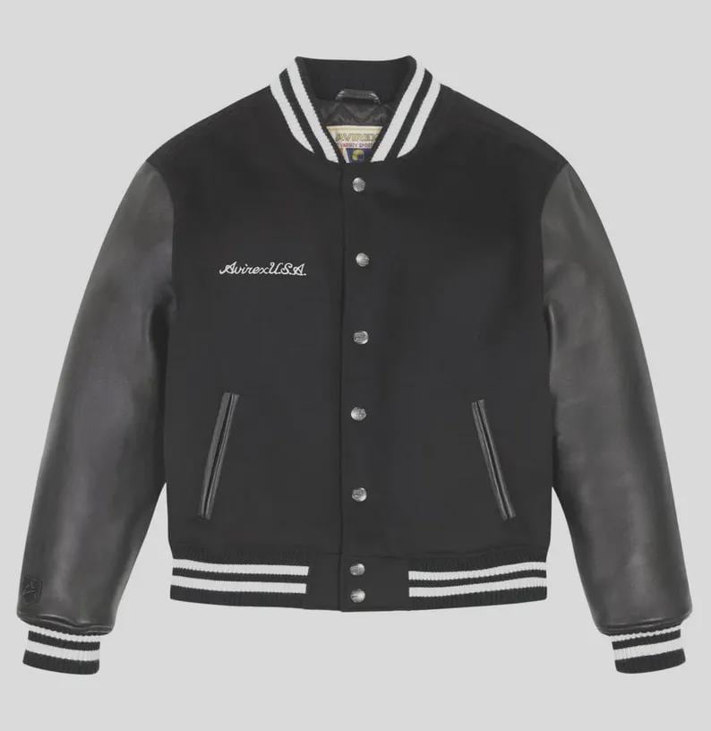 Op de afbeelding: Een zwart varsity-jack met zwarte leren mouwen en een zwarte body van wolmix. Het jack heeft een drukknoopsluiting, twee zijzakken en wit gestreepte geribbelde boorden bij de kraag, mouwen en zoom. AvirexUSA is in het wit op de borst geborduurd.