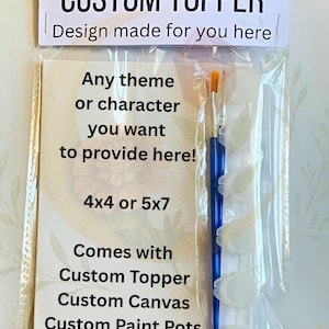 Op de afbeelding: Een doorzichtige plastic verpakking met een op maat gemaakte topper kit. De kit bevat een canvas, verfpotten en penselen. Tekst op de verpakking luidt "CUSTOM TOPPER" en "Design made for you here".