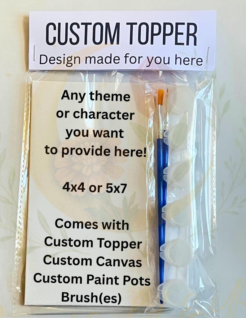 Op de afbeelding: Een doorzichtige plastic verpakking met een op maat gemaakte topper kit. De kit bevat een canvas, verfpotten en penselen. Tekst op de verpakking luidt "CUSTOM TOPPER" en "Design made for you here".