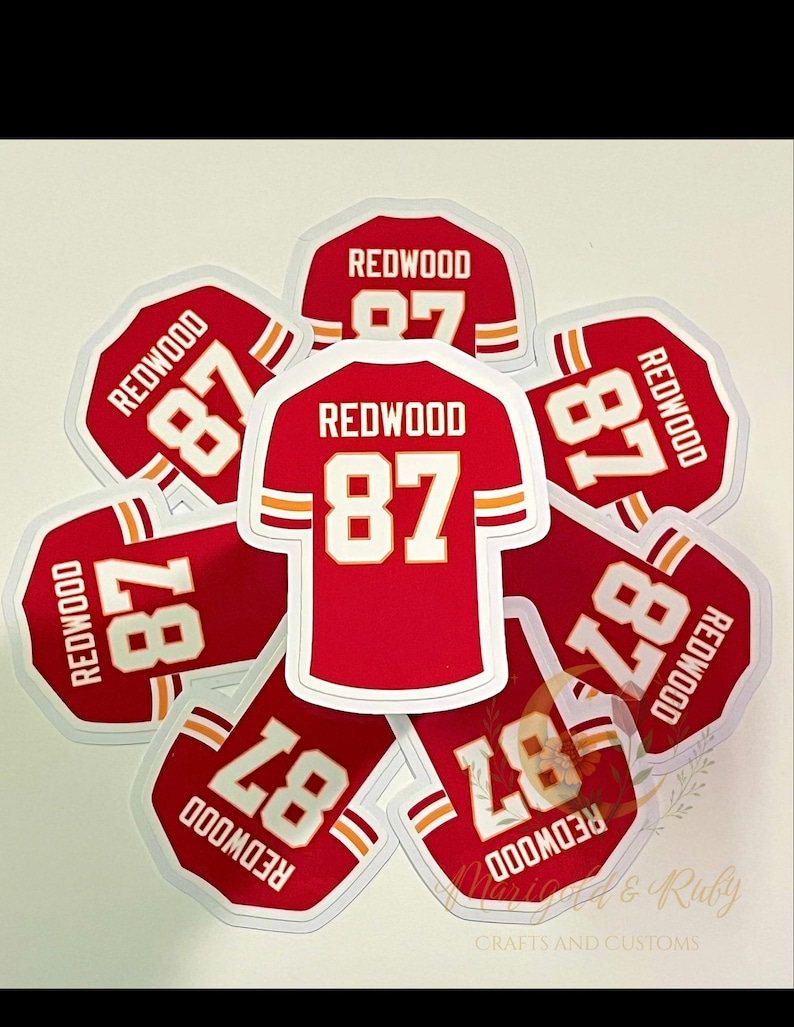 Red football jersey sticker with “REDWOOD 87,” inspired by Taylor Swift’s Life of a Showgirl “wood” song and Travis Kelce. Features white and yellow sleeve stripes and a glossy laminated finish.