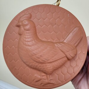 May include: A terracotta ceramic chicken mold with a honeycomb pattern. The mold has a loop for hanging.