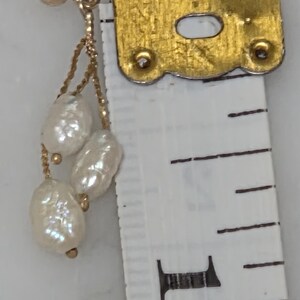 May include: A gold-toned earring with three white, irregularly shaped pearls dangling from a delicate chain. The earring is next to a measuring tape, showing the size of the pearls.