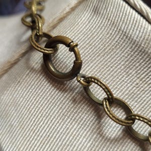 Pu&ograve; includere: Primo piano di una collana a catena dorata con chiusura a moschettone. La catena &egrave; composta da piccoli cerchi collegati.