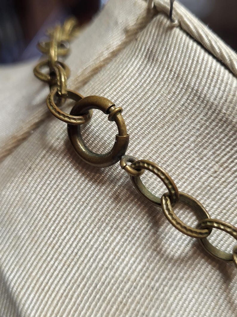 Pu&ograve; includere: Primo piano di una collana a catena dorata con chiusura a moschettone. La catena &egrave; composta da piccoli cerchi collegati.