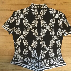 Puede incluir: Top de manga corta negro y blanco con un patr&oacute;n floral. El top tiene un cuello alto y una silueta ajustada.