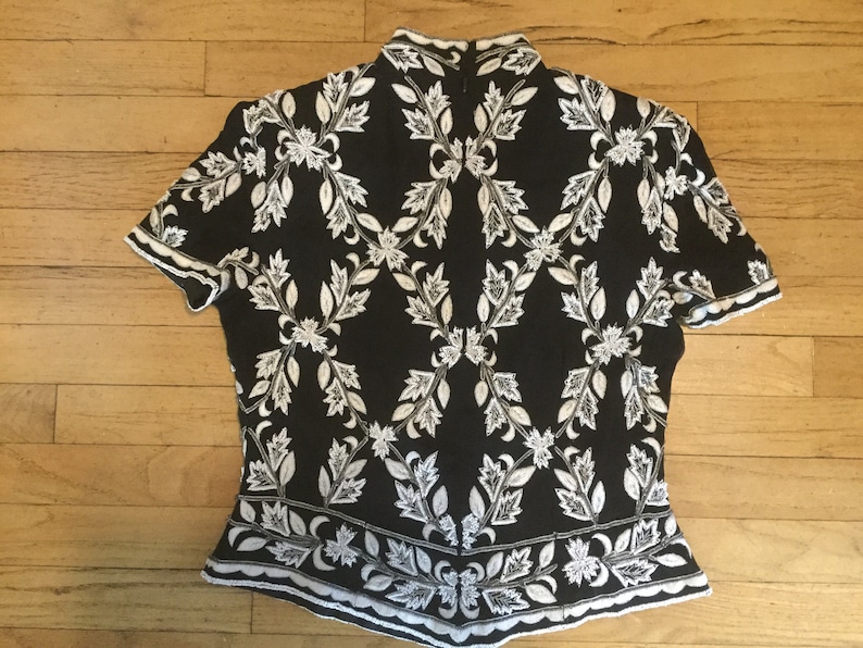 Puede incluir: Top de manga corta negro y blanco con un patr&oacute;n floral. El top tiene un cuello alto y una silueta ajustada.