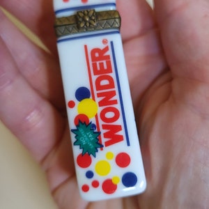 May include: White ceramic box with a hinged lid and a gold-colored metal clasp. The box is decorated with red, blue, and yellow circles and the word "WONDER" in black lettering. The box also has a green starburst with the text "NO SATURATED FAT" in white lettering.