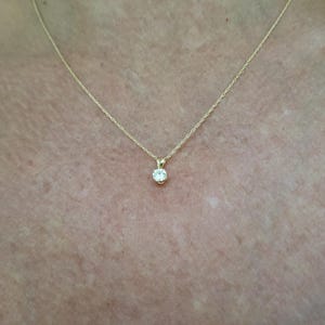 May include: A simple gold chain necklace with a small, round, clear gemstone pendant.