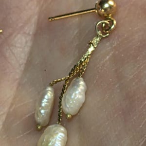 May include: A gold-colored earring with three dangling, irregularly shaped white pearls. The earring has a post and a small gold ball at the top. The pearls are attached by a delicate gold chain.