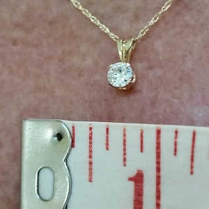 May include: A gold chain necklace with a small, round, clear gemstone pendant. The pendant is about 1 inch in diameter.