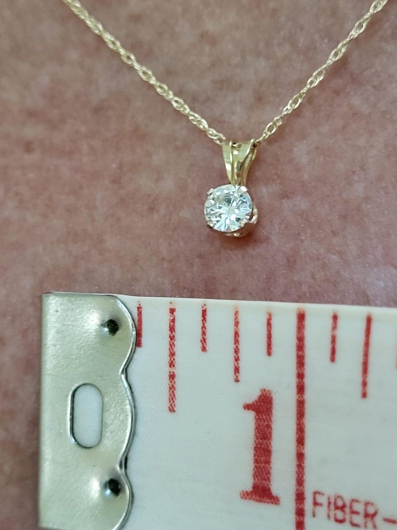 May include: A gold chain necklace with a small, round, clear gemstone pendant. The pendant is about 1 inch in diameter.