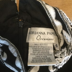 Puede incluir: Vestido negro de seda con bordados blancos y plateados. El vestido tiene una etiqueta que dice "Adrianna Papell Occasions" e incluye instrucciones de cuidado. La etiqueta de talla indica la talla 8.
