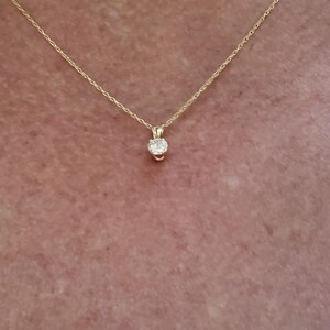 May include: A delicate gold chain necklace with a small, round, clear gemstone pendant.
