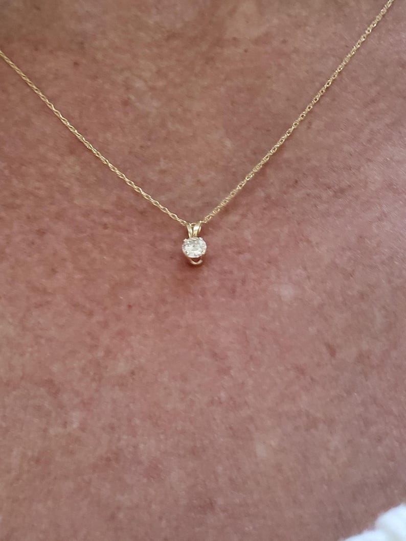 May include: A delicate gold chain necklace with a small, round, clear gemstone pendant.