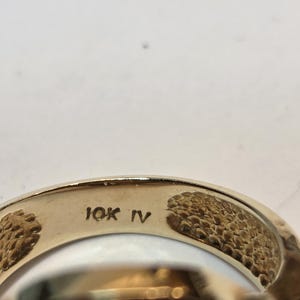 May include: Close-up of the inside of a gold ring with the inscription "10K IV" on the band.